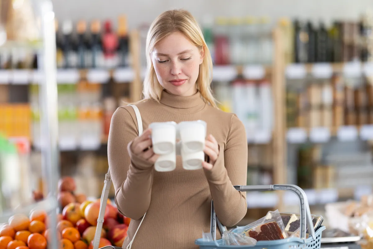 Egy nő épp a termékek összetevőjének listáját nézi, hogy lekerülje, hogy egészségtelen ételeket vegyen.