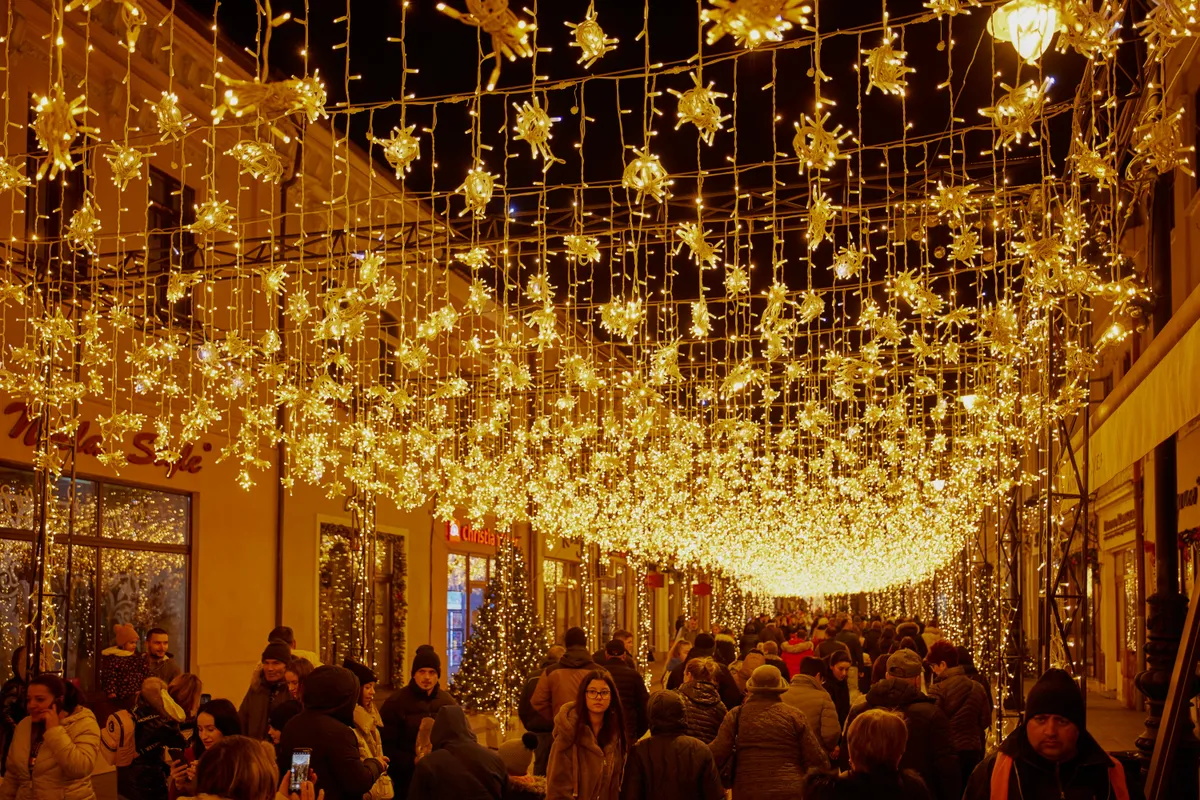 Emberek fényfüzérek alatt sétálnak Európa legnagyobb karácsonyi vására helyszínén
