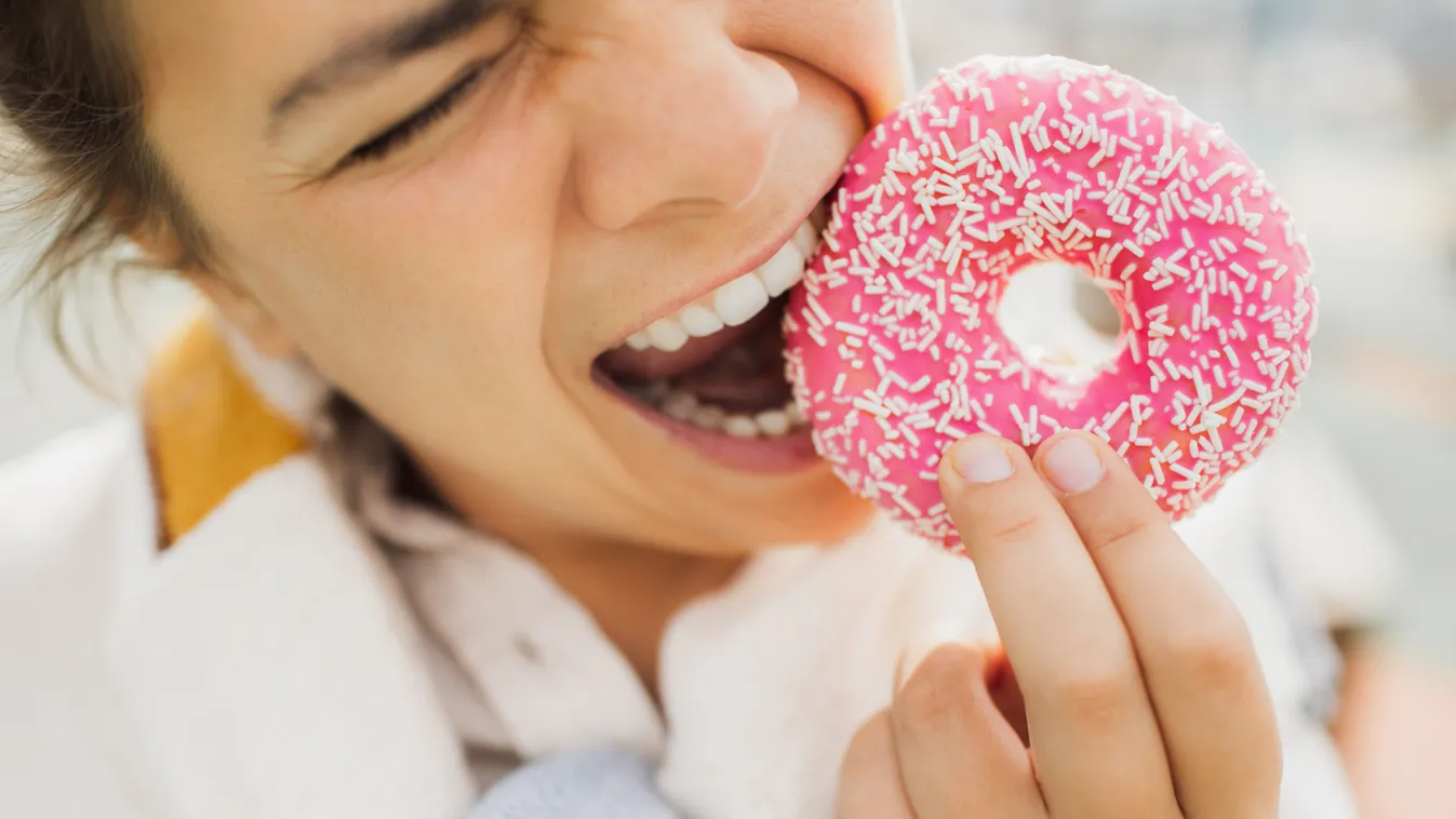 Fánkba harapó nő, aki nem tartja be a diétát.