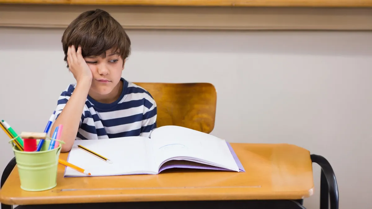 Biológiai kvízt író kisfiú az iskolapadban.