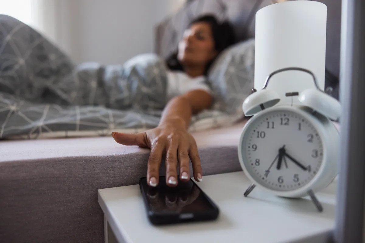 Ébresztőóra jelzése miatt a telefonjához kapó nő az ágyban