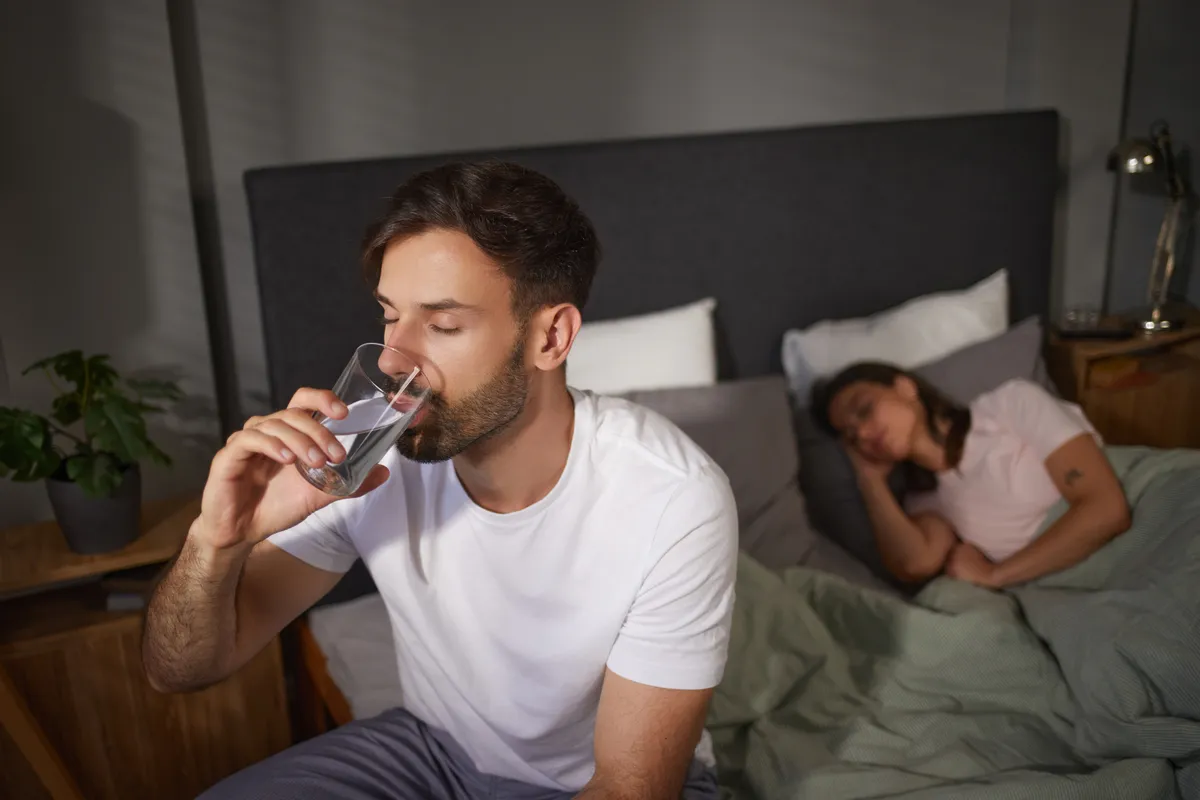 fiatal férfi vizet iszik reggel az ágy szélén, hpogy kaprban tartsa a szívét. 