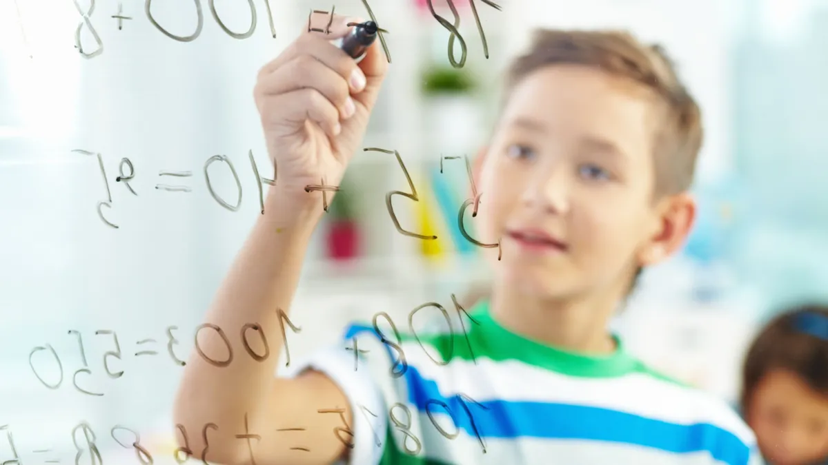 Egy fiú épp a matek kvízünk egyik kérdését próbálja megoldani egy üvegtáblán.