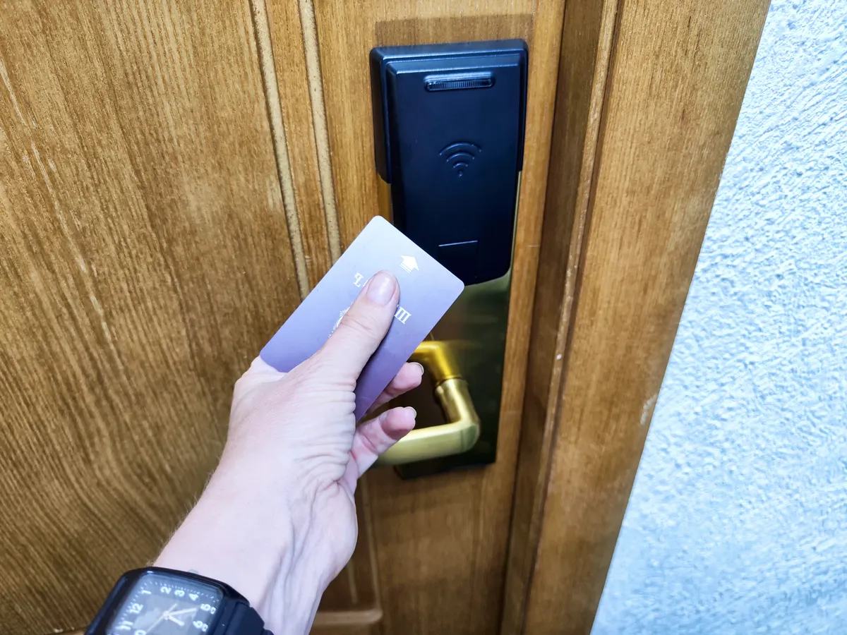 női kéz szállodaiszoba zárjánál, miközben egy belépőkártyával nyitja az ajtót.