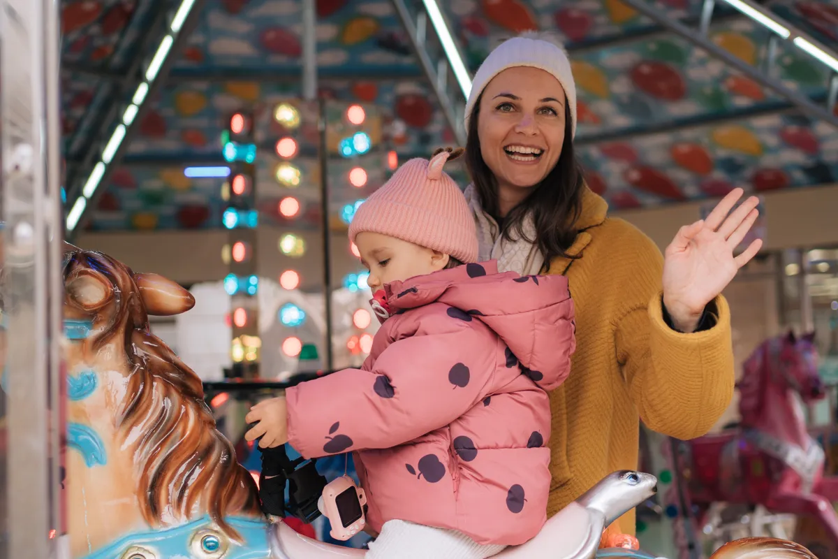 Vidámparkban körhintán ül téli ruhában egy édesanya a gyermekével.