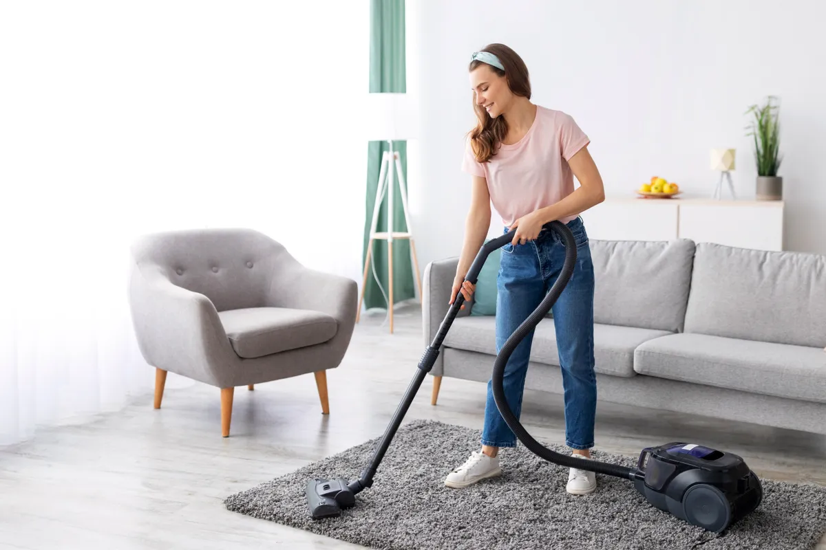 egy nő vezetékes porszívóval takarít. 
