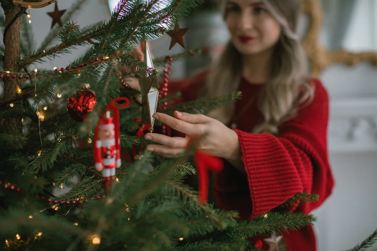 Karácsonyi divat szerint felöltözött fiatal lány fát díszít.