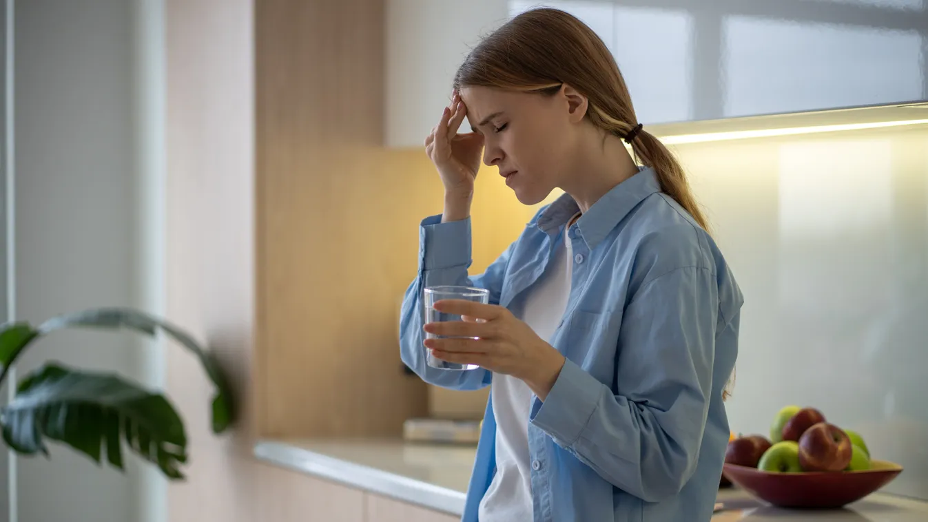 Fejfájás megelőzése érdekében vizet ivó fiatal nő a konyhában
