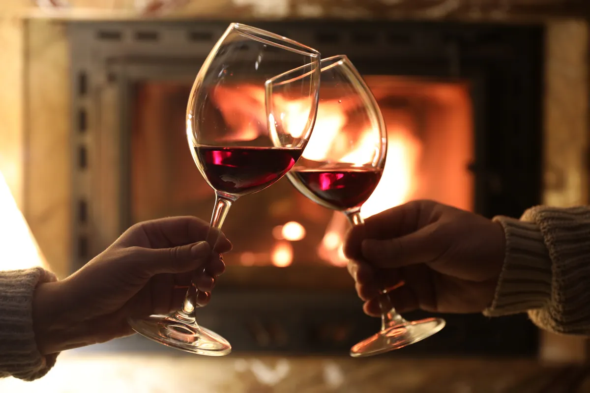 vörösborral koccintó pár keze, háttérben egy kandalló.