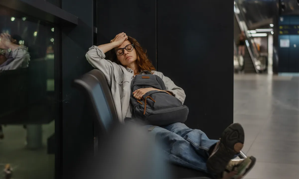 fiatal nő bóbiskol egy reptéri váróban, kezében a hátizsákjával.