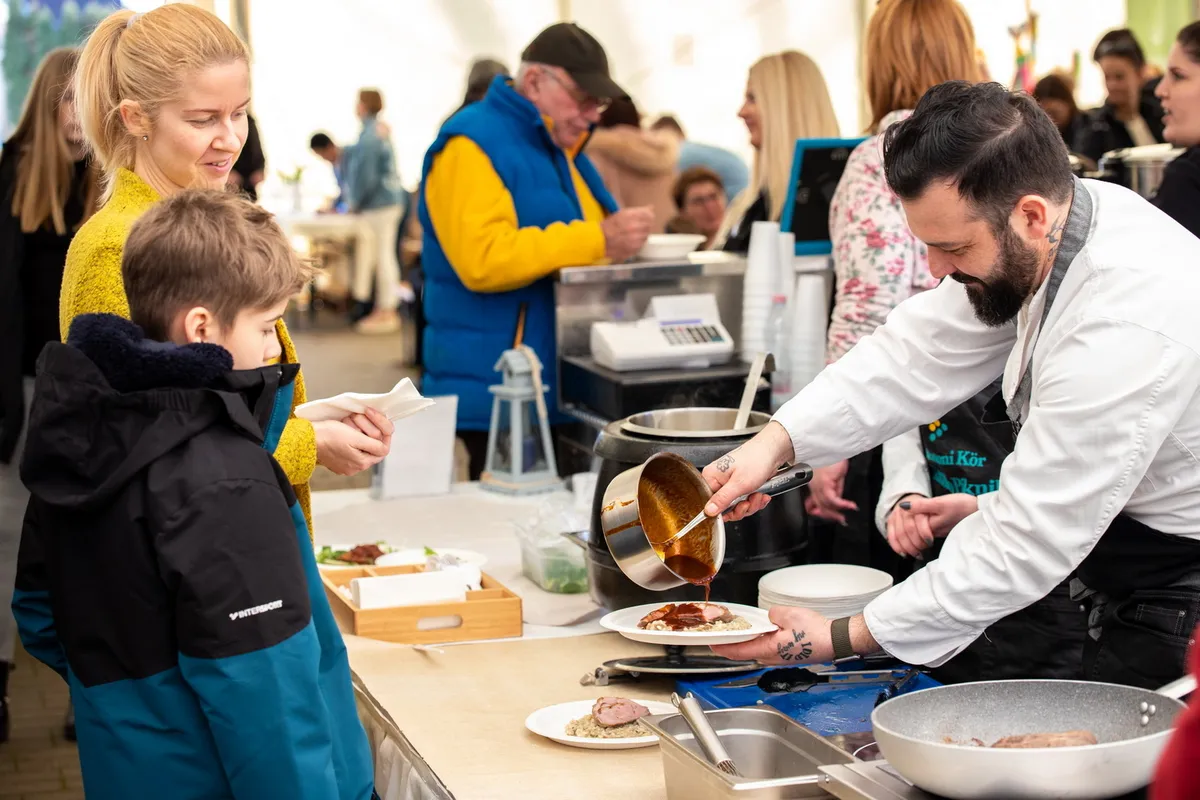 Egy nő és a fia nézik, ahogyan a séf tálalja nekik az ételt a balatonlellei gasztro farsangon