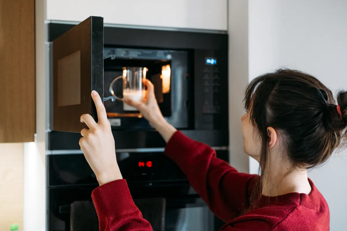 Mit nem szabad mikróba tenni: fiatal nő egy pohár tejet tesz a mikróba