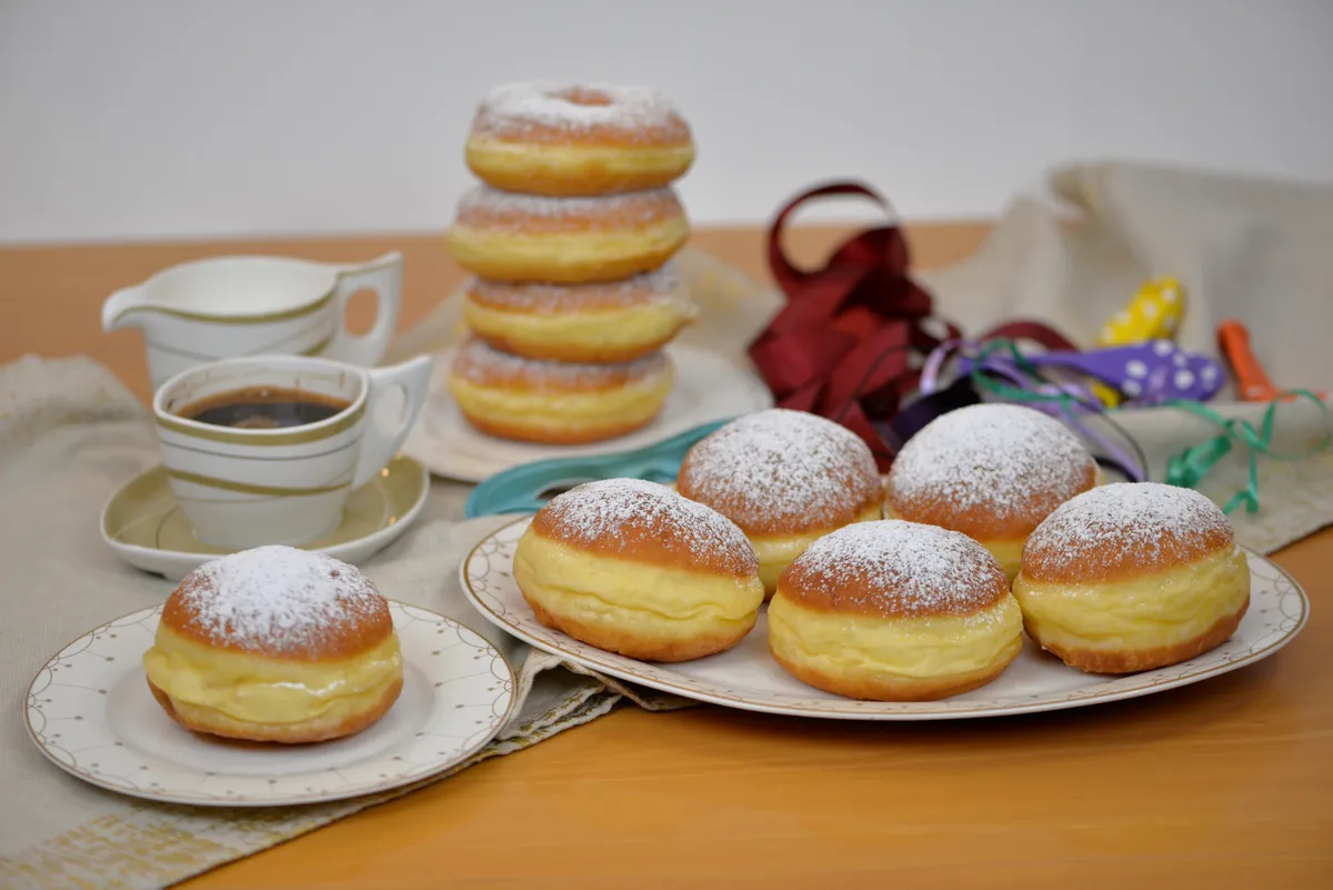 A farsangi fánk története: szalagos fánkok tányérokon, mellettük kávés csésze és farsangi dekorációk