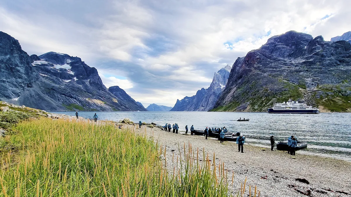 A Prince Christiane Sound fjord turistákkal, partra húzott gumicsónakokkal, hajóval és füves zöld partszakasszal.