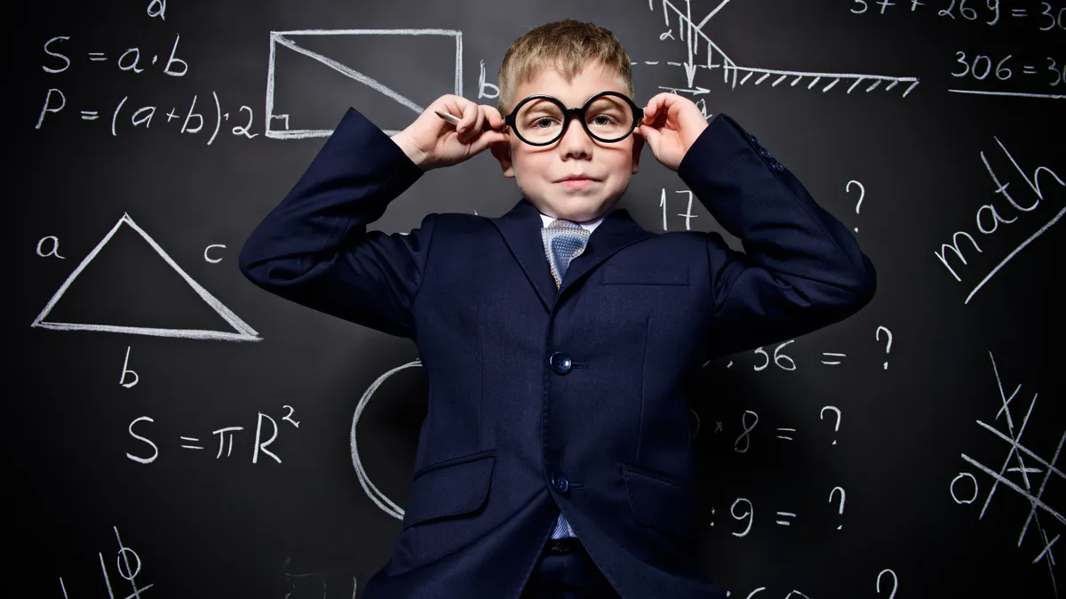 Egy matematikai feladványokkal teli tábla előtt áll egy kisfiú, aki büszke, mert megoldotta a matek kvízt. 