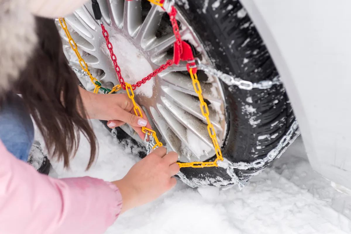 Egy nő épp a hólánc felszerelése közben.