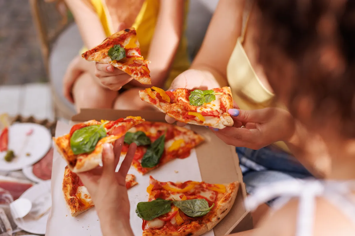 Női kezek pizzaszeleteket tartanak egy pizzás doboz felett a városban, ahol a legolcsóbb pizza kapható.