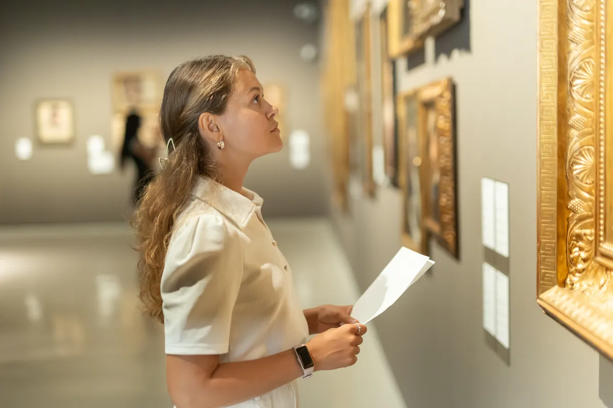 Egy nő a galériában épp a festményeket nézegeti, mert a művészettörténeti kvízünket tölti.