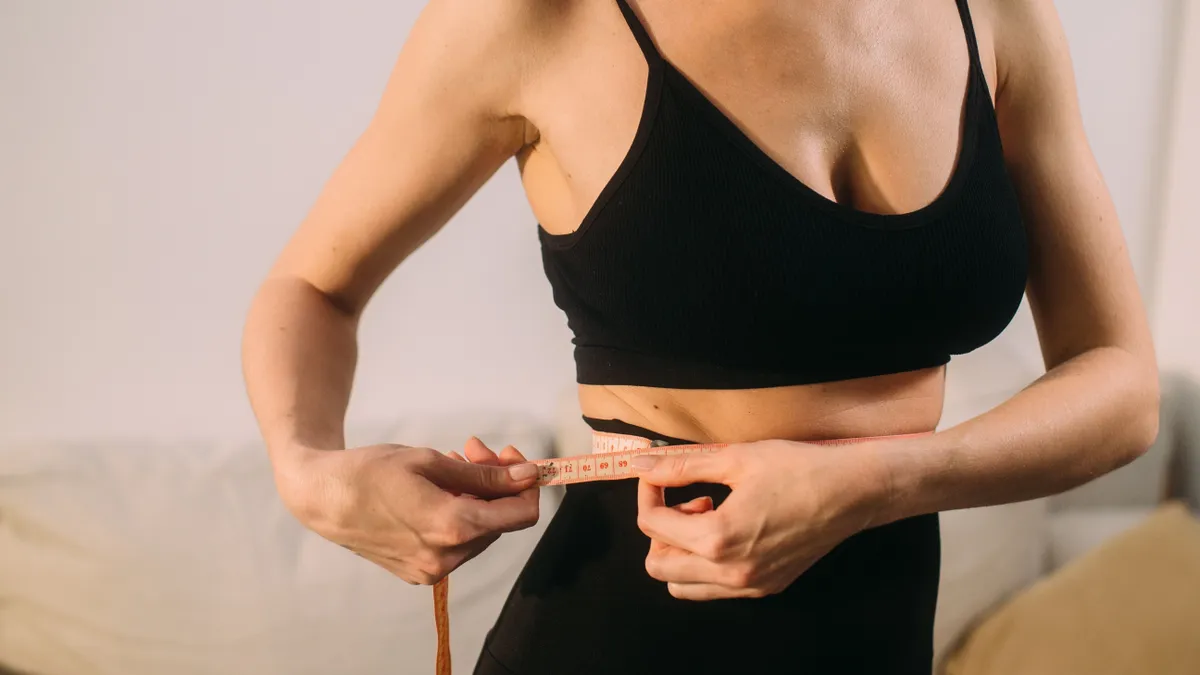Fogyókúrás tapaszt használó nő épp méri a derekát.