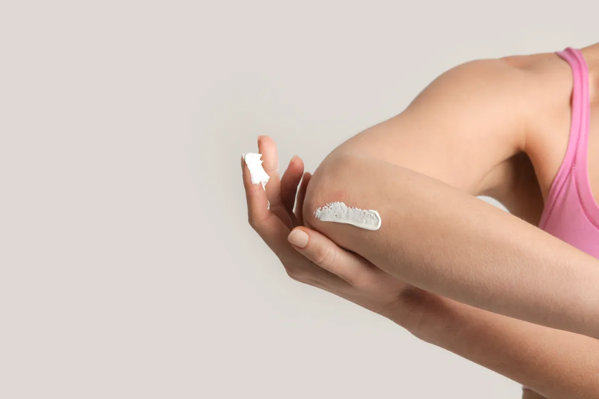 Téli bőrvédelem részeként a könyökét testápolóval kenő nő