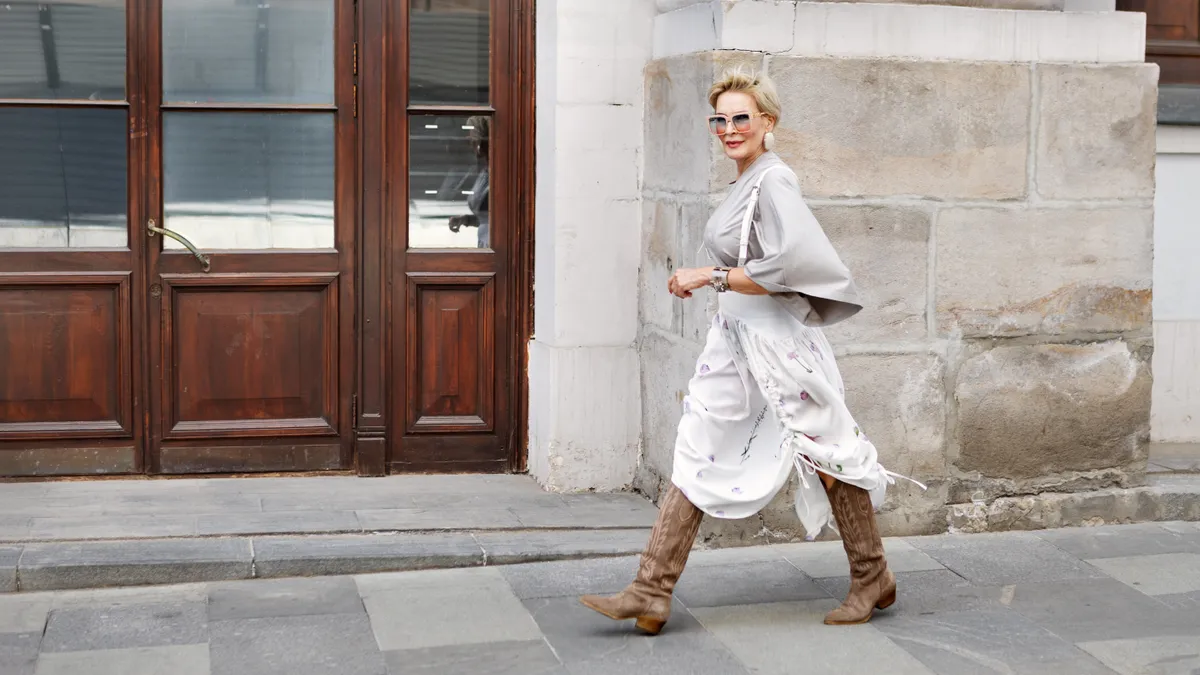 Barna velúr csizma egy divatosan öltözködő idős hölgyön, aki épp sétál.