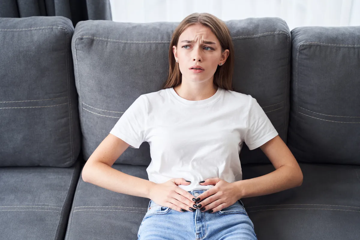 Egy fiatal nő a kanapén fekszik, endometriózis miatt fájdalami vannak.