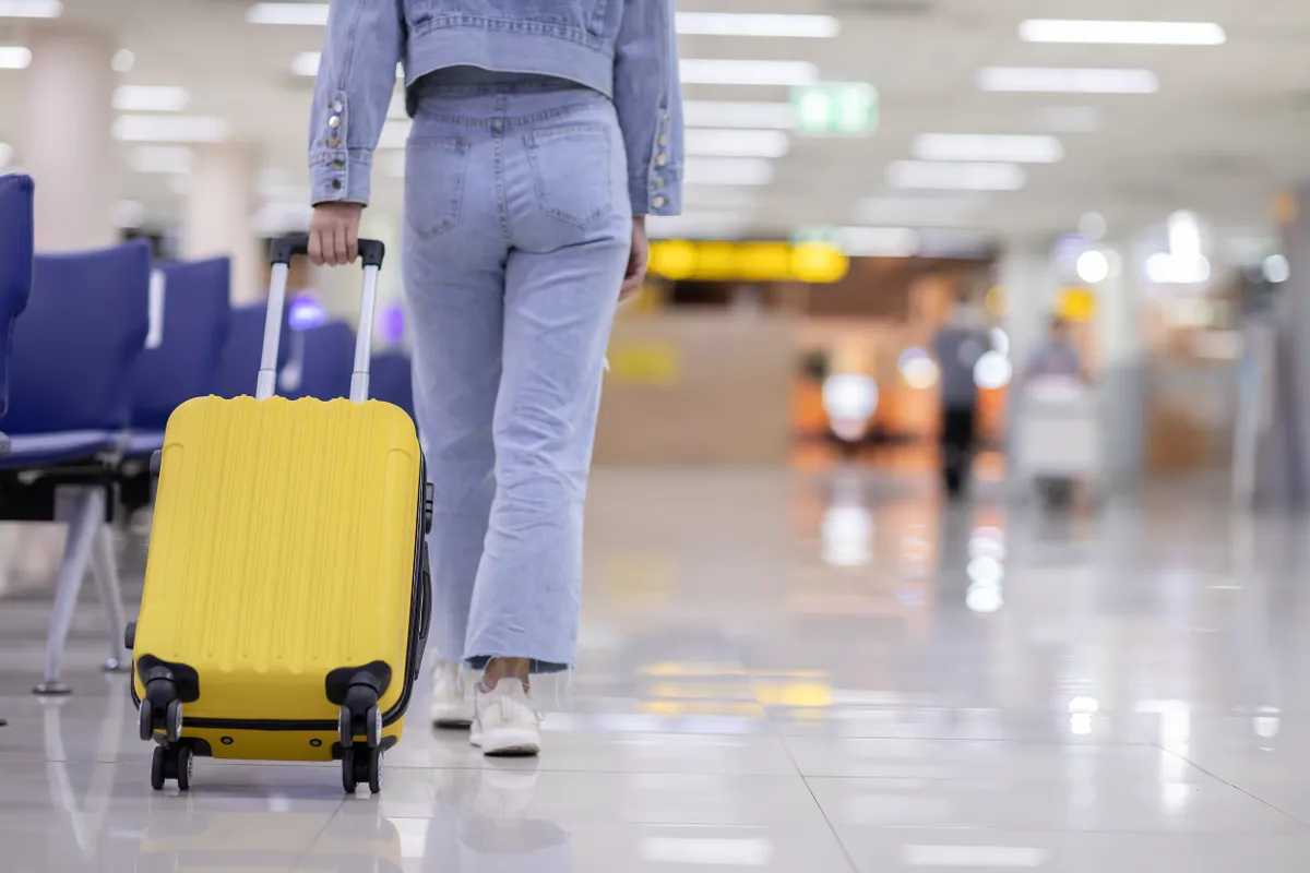 Nő sárga bőröndöt húz egy repülőtéren.