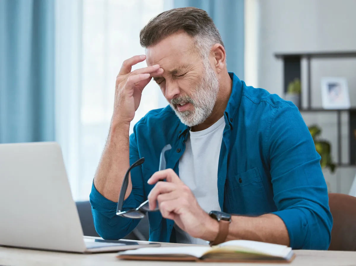 Stresszes fejfájást tapasztaló férfi munka közben a laptop előtt.