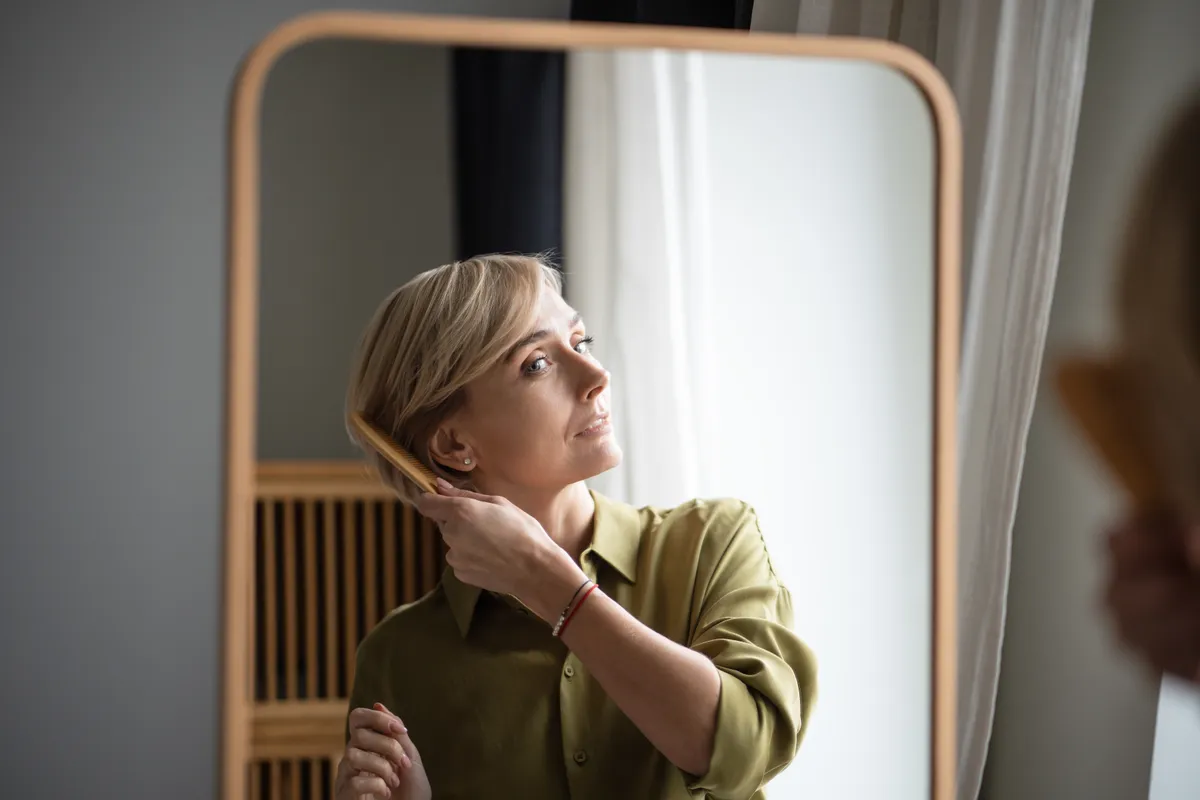 50 feletti nő csinálja a tükörben a haját.