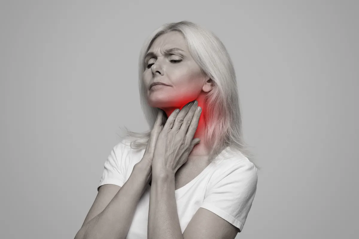 Egy nő fogja a nyakát, torokrákja van.