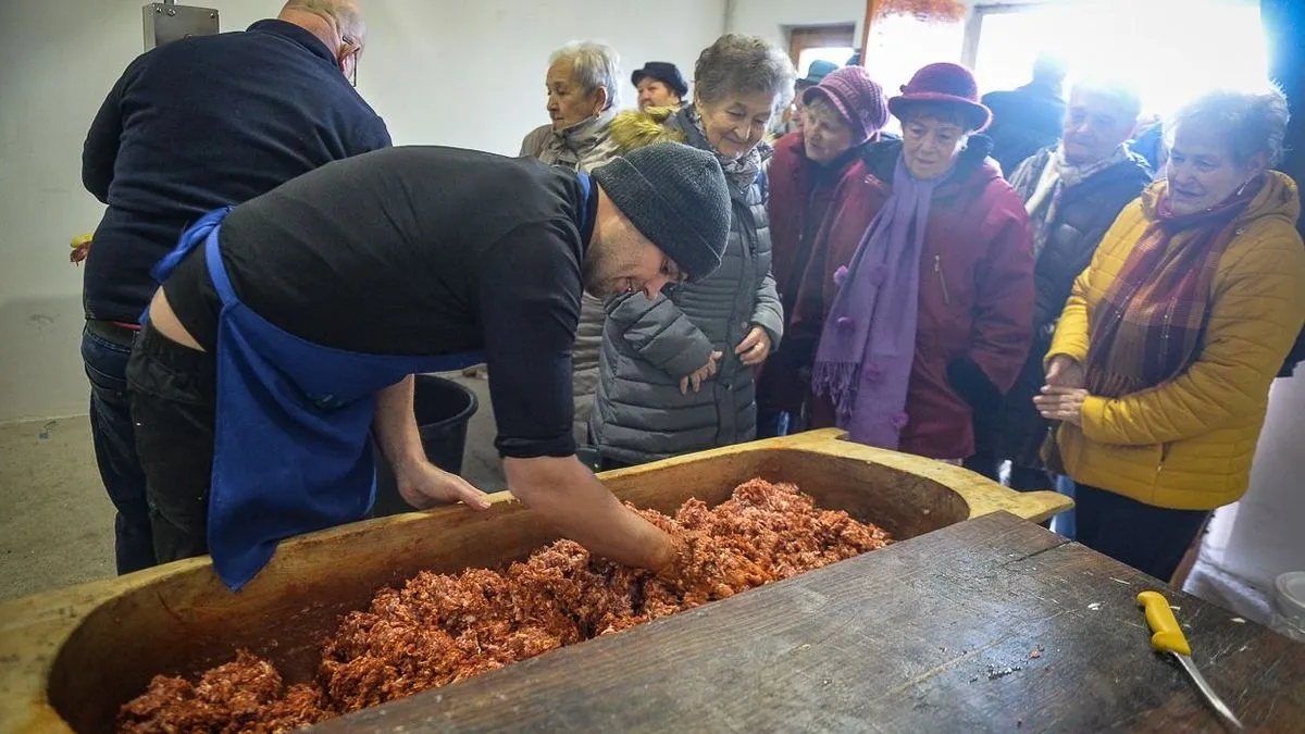 Nyilvános disznóvágás, amin egy férfi fa teknőben keveri be a kolbásznak valót.