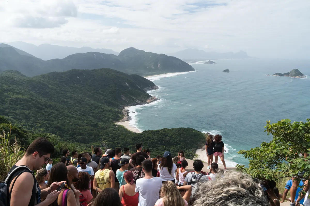 gyönyörű tengerparti környezetben, meredek sziklákon fotózkodó páros, miközben nagy tömeg vár a sorára. 