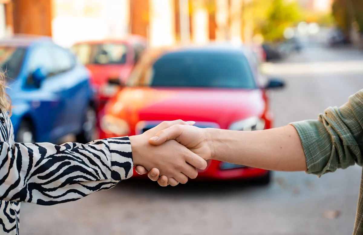 Használt autó vásárlás előtt kezet rázó nő és férfi.