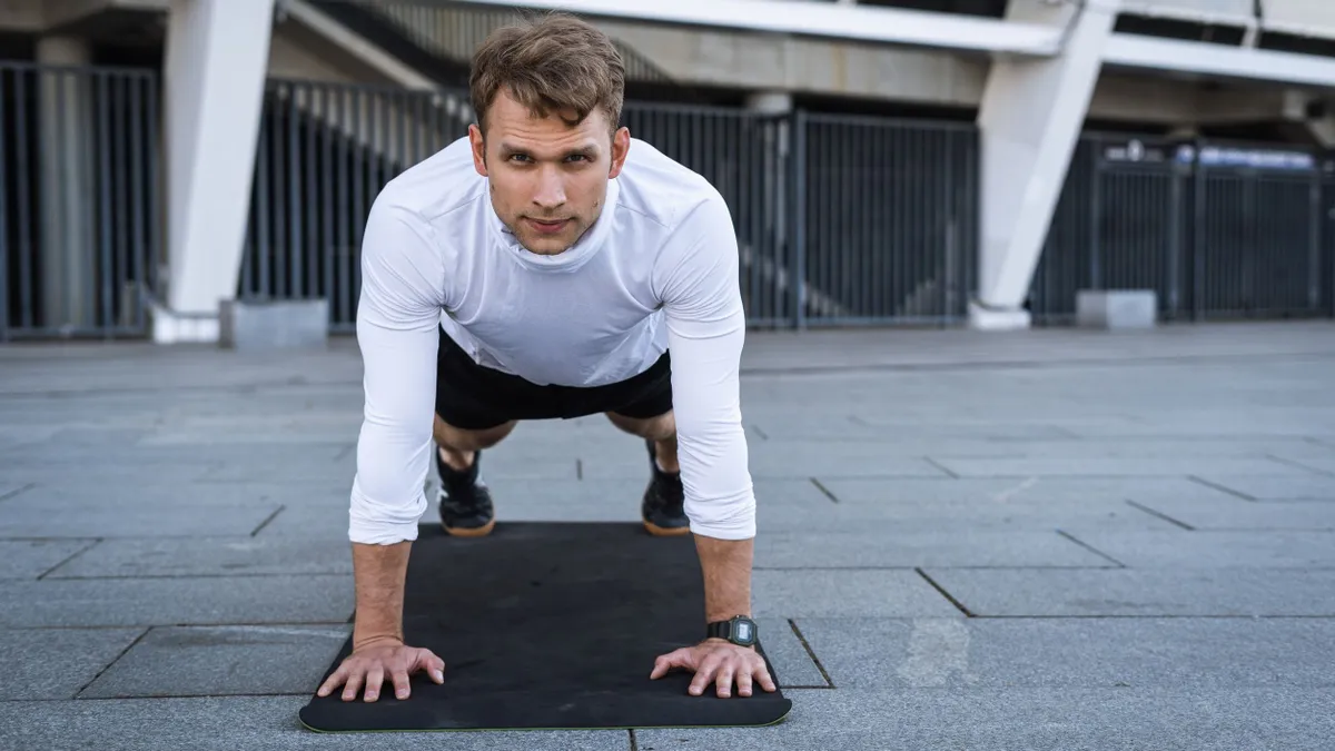 Sportive man training outdoors, standing in plank pose