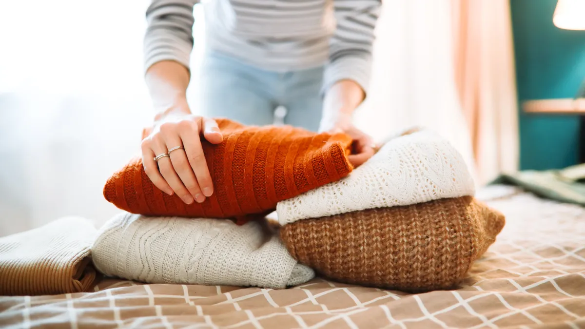 Kötött pulóvereket hajtogató nő.