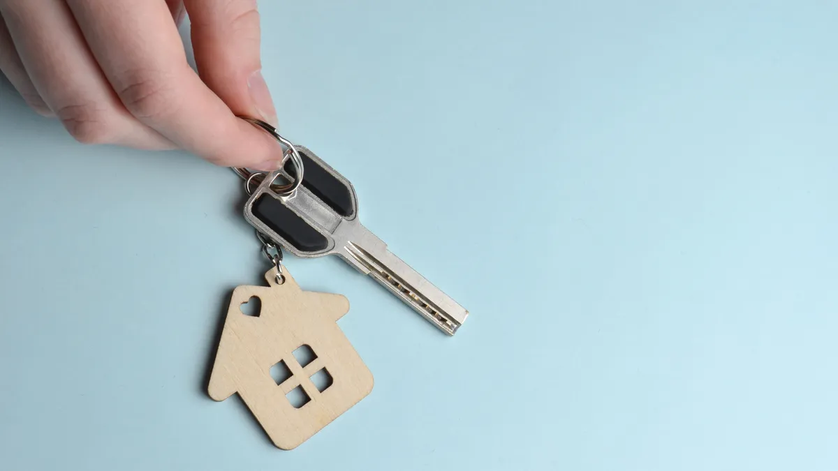 Wooden keychain in the shape of a house and a key in hands on a blue background.
