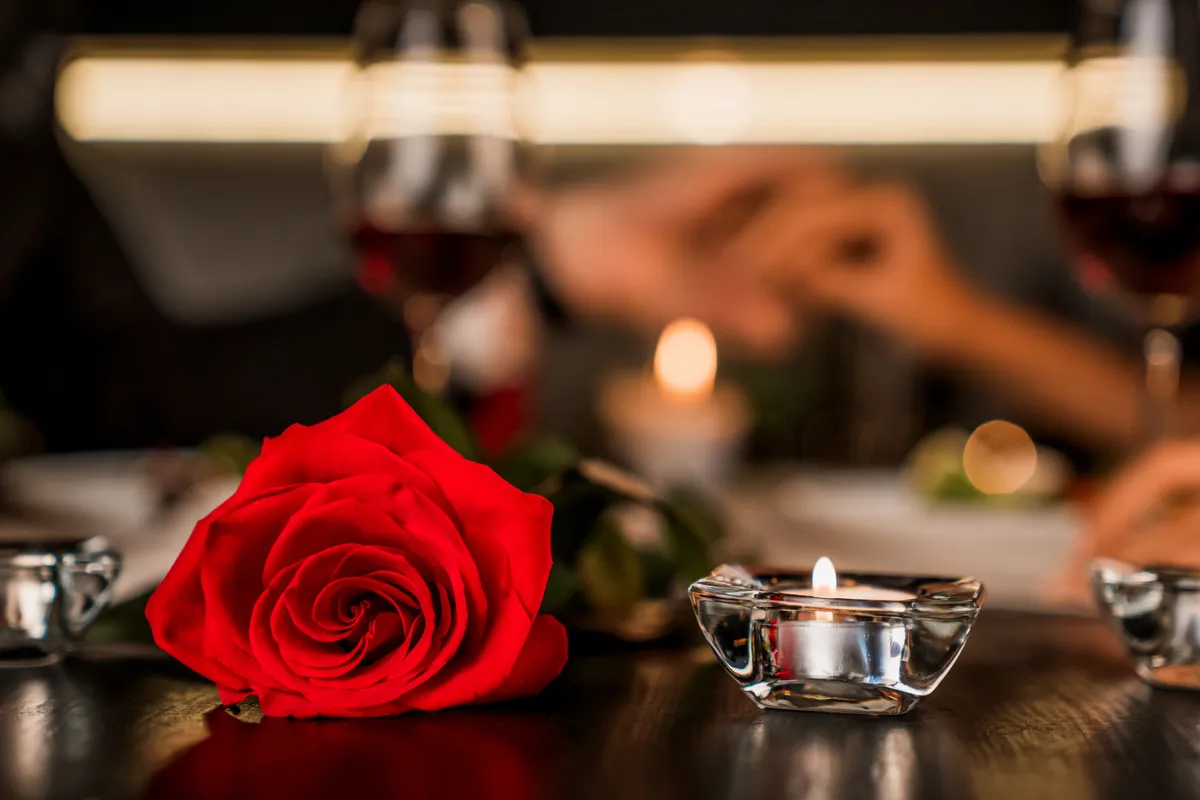 Valentin-napi rózsa és égő gyertya az asztalon.