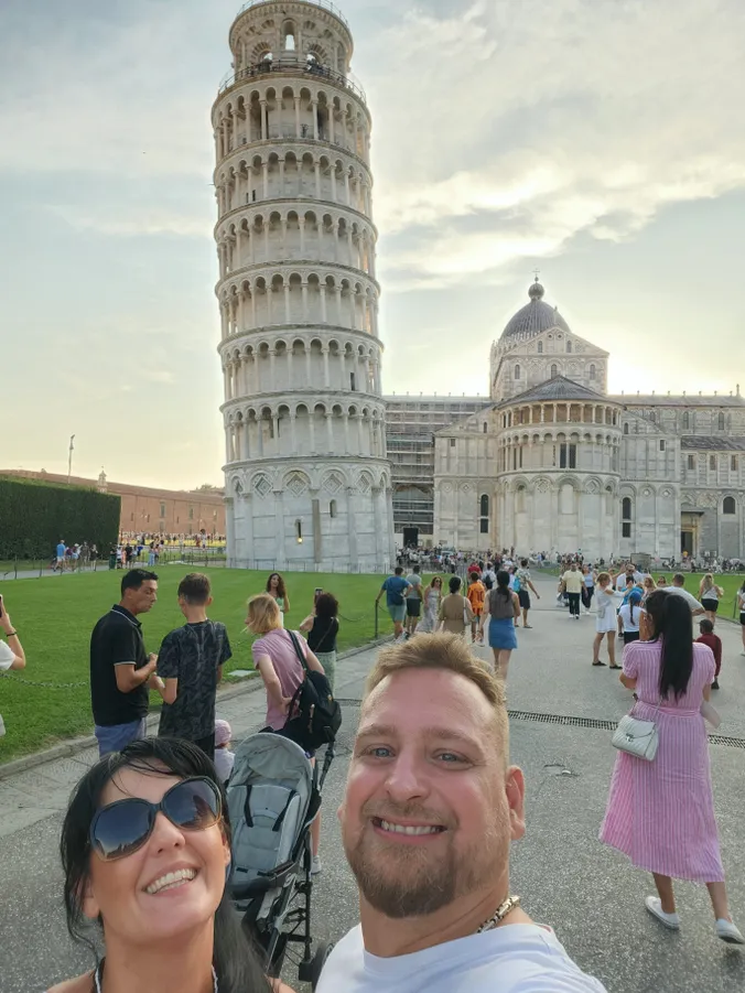 olaszországi nászúton lévő pár a pisai ferde torony előtt szelfizik.