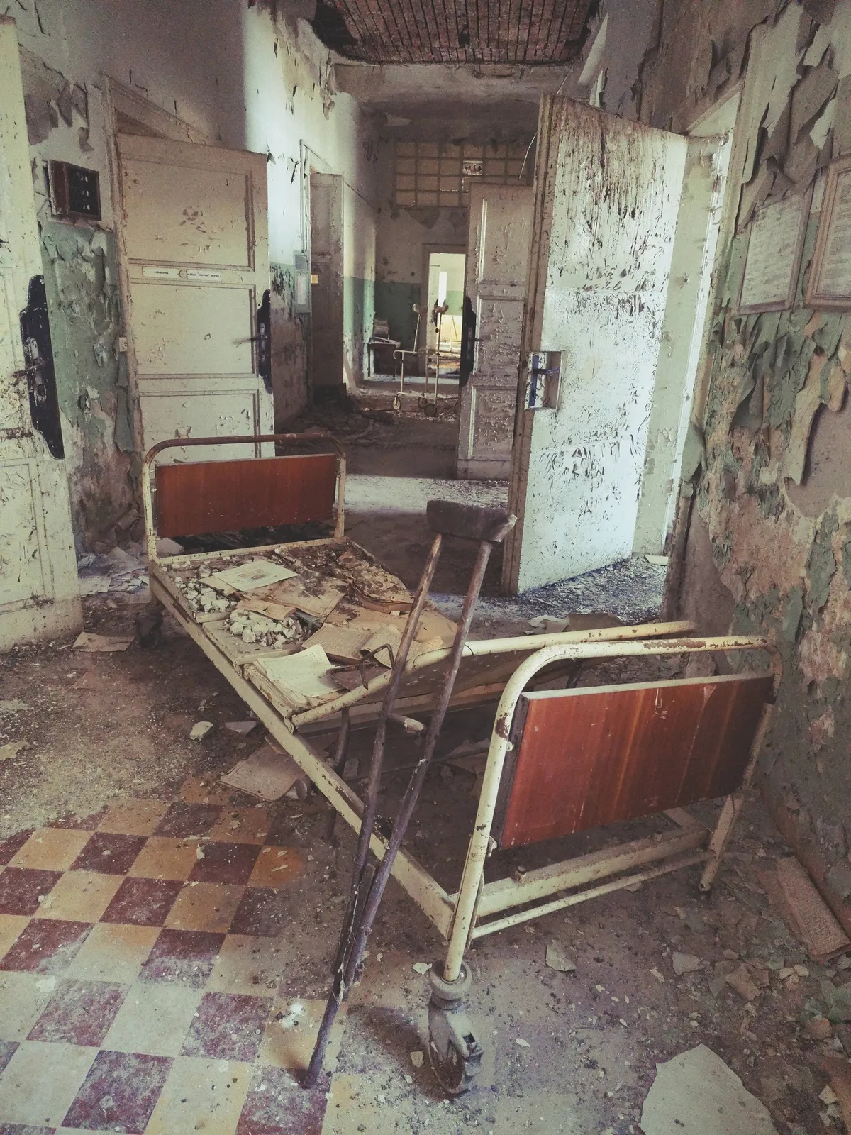 Elhagyatott kórház porlepte berendezési tárgyai, ágy, mankó, iratok.