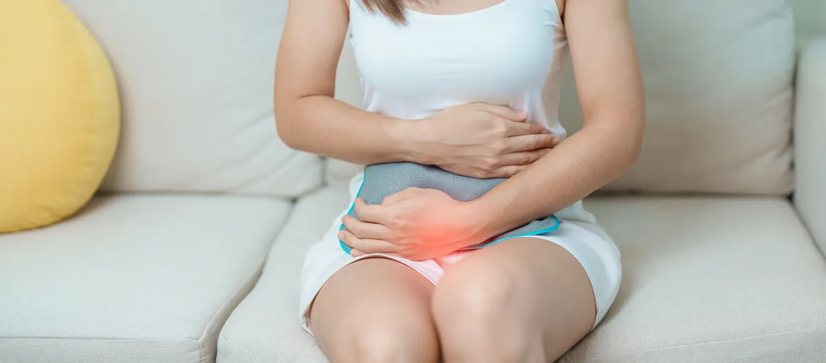 A menstruációs fájdalom ellen melegítőpárnás kezelést alkalmazó nő ül a kanapén.