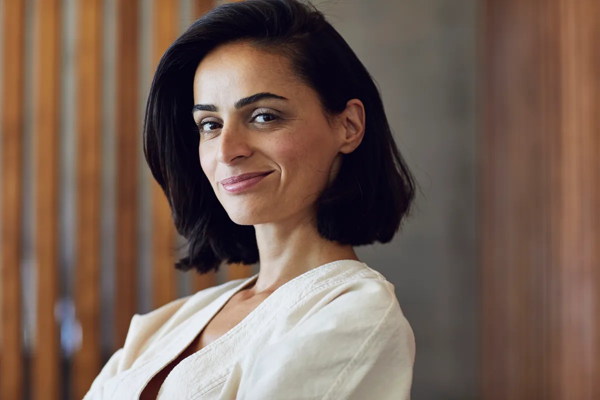 Fekete hajú nő önbizalommal telien mosolyog.