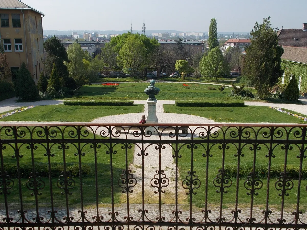 A budai arborétum felső kertje, középen egy szoborral egy korlát mögül nézve.