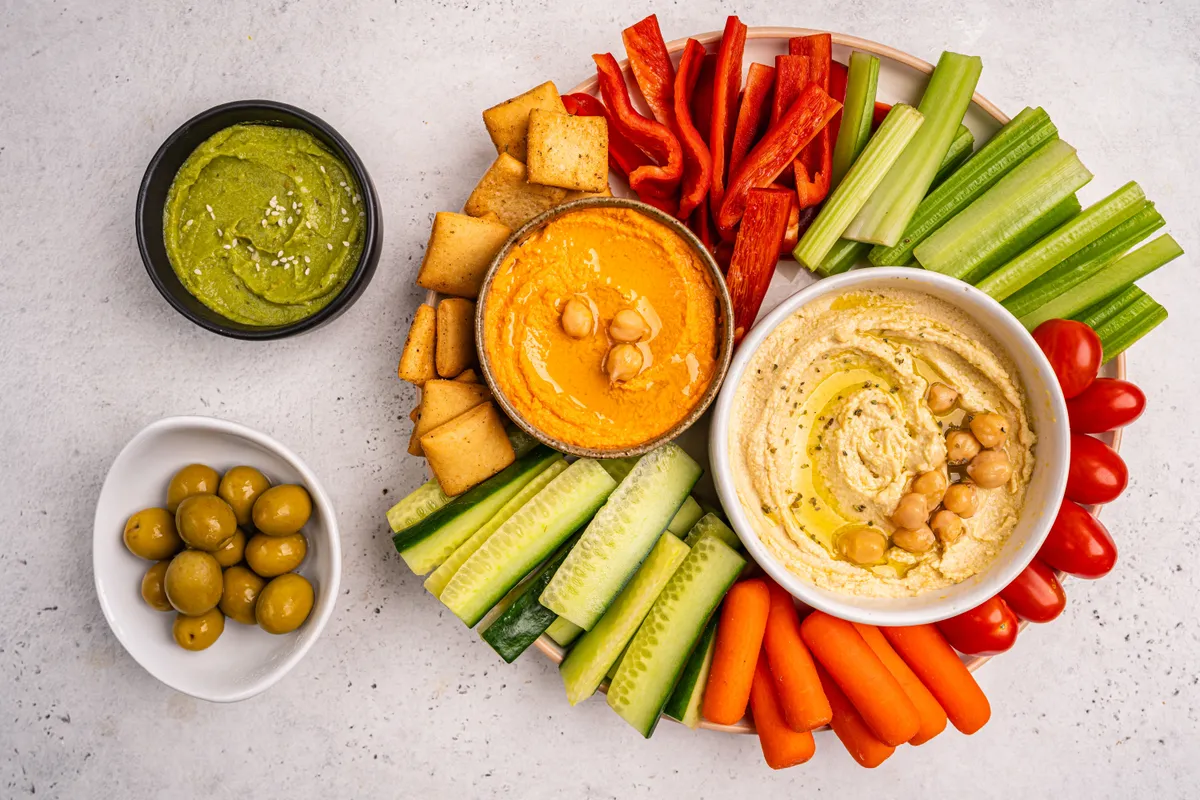 Különféle hummuszok és mártogatósok tálban, csíkokra vágott zöldségekkel