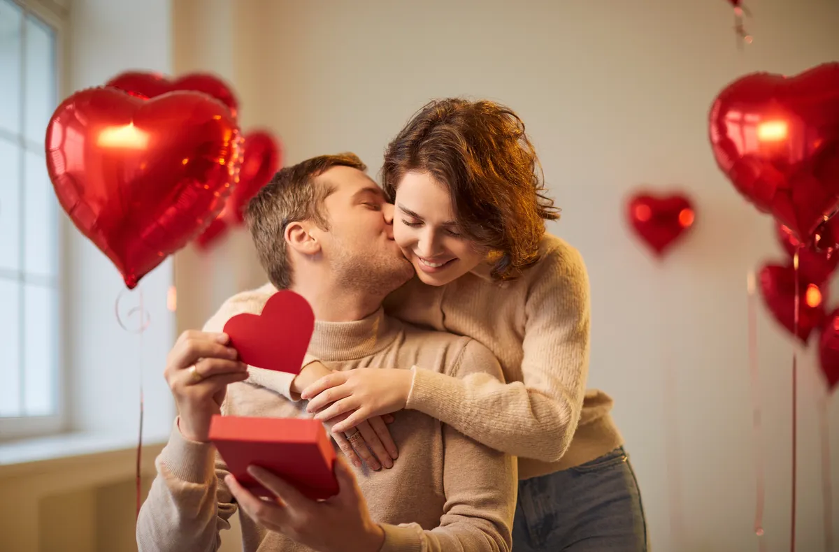 Átadott ajándékok Valentin-napra: fiatal nő átöleli a párját, a háttérben piros lufik.