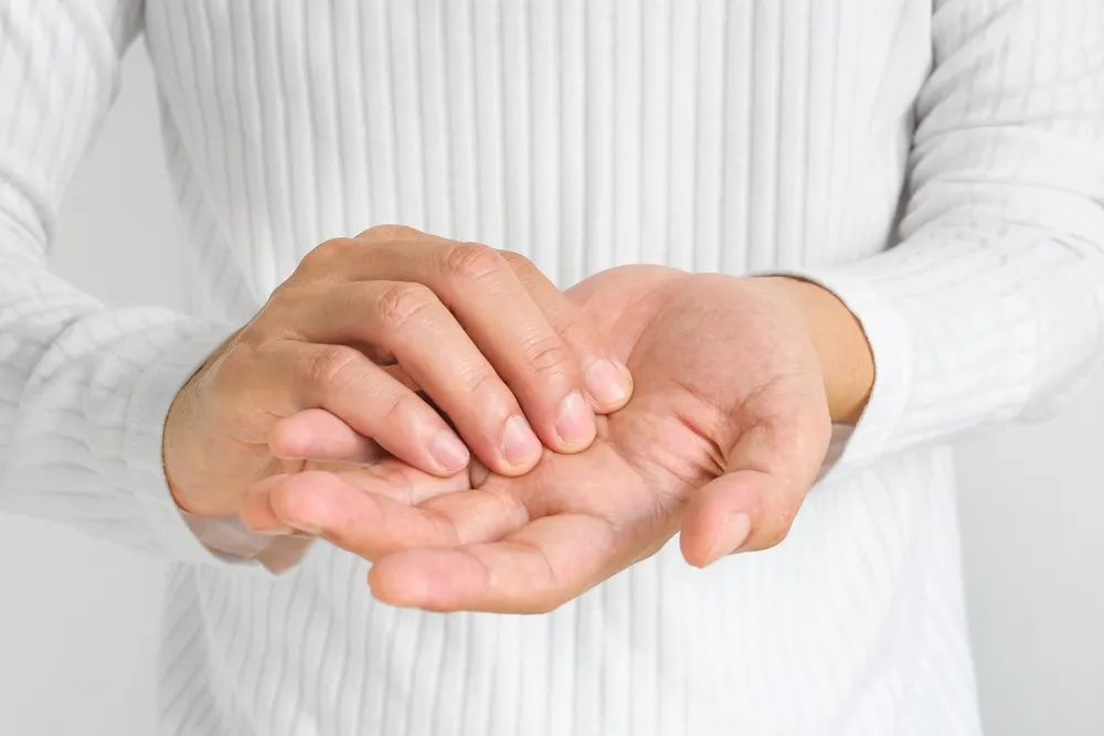 Kézzsibbadás tüneteit észlelő nő a tenyeréhez nyúlva
