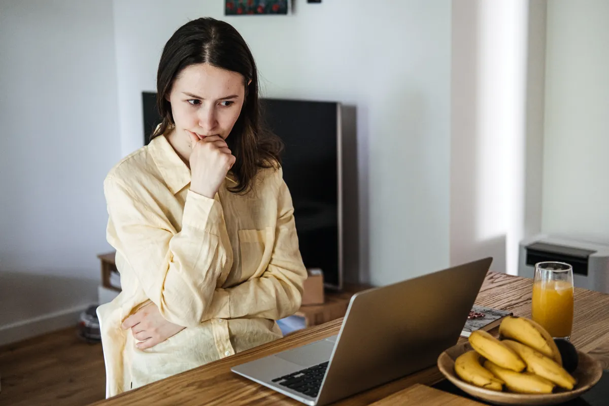 Fiatal nő online tanfolyamot keres a laptopján egy asztalnál ülve.