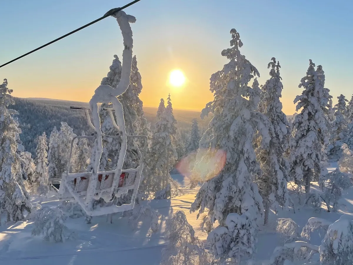 Kilátás a sífelvonóról Lappföldön alacsonyan álló Nappal és hóborította fákkal. 