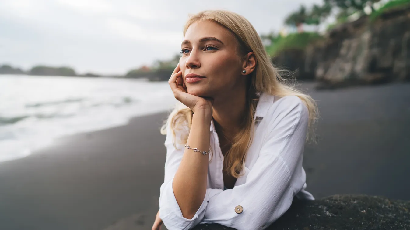 Öreg lélekkel rendelkező fiatal szőke nő a tengerparton borús időben