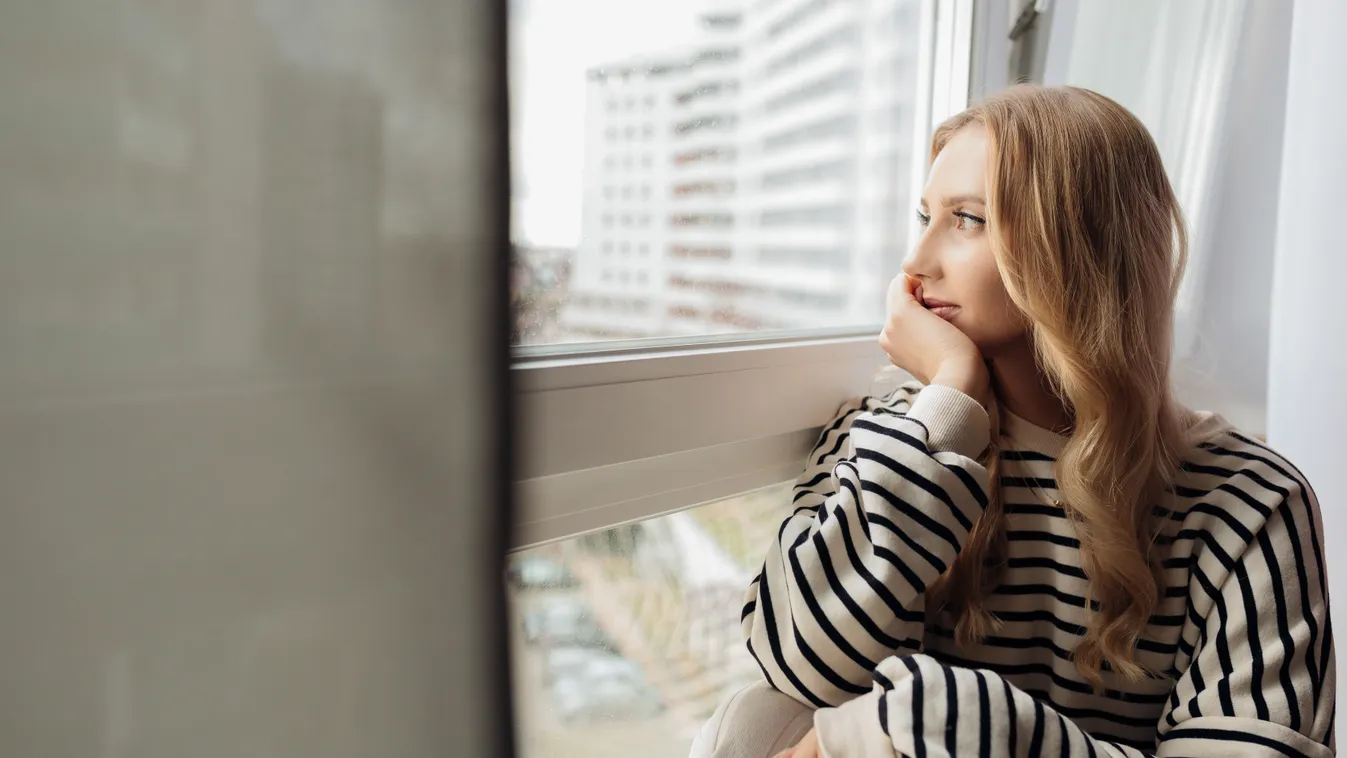 Ablakon kinéző fiatal nő, aki érzi, milyen hatalmas a gondolatok ereje