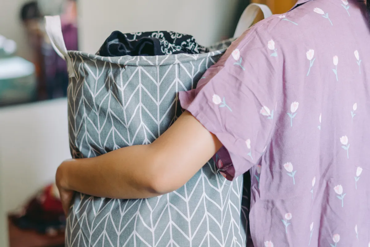 Szennyeskosarat tartó fiatal nő pizsamacsere után